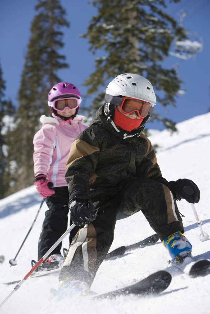 Children skiing downhill with helmets and goggles