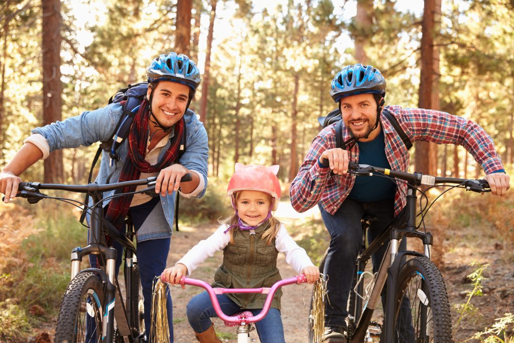Male couple biking with child wearing helmets